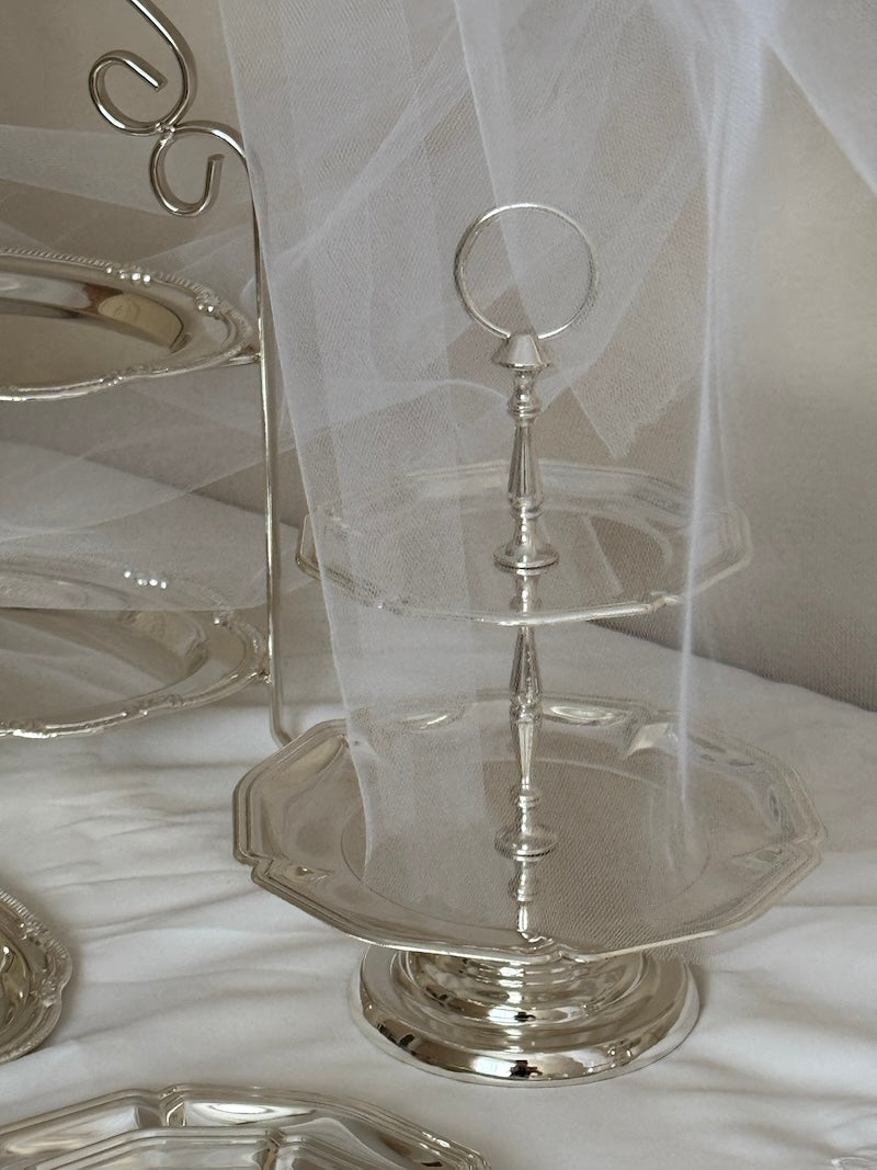 Silver three-tiered stand on tabel cloth with a white curtain in the background