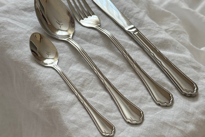 Set of silver cutlery including a knife, fork, and two spoons on a white fabric background.